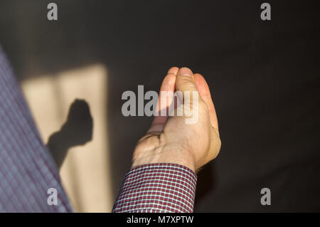 La main de l'homme avec les doigts pliés dans une pincée, une ombre sur le mur à la main Banque D'Images