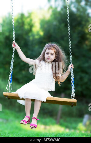 Belle petite fille assise sur la balançoire à jour d'été, enfance heureuse concept Banque D'Images