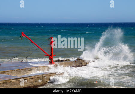 La grue rouge sur le quai avec l'état de la mer Banque D'Images