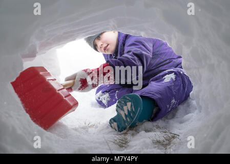 Jeune canadienne à creuser le tunnel de la neige avec une pelle en plastique rouge Banque D'Images