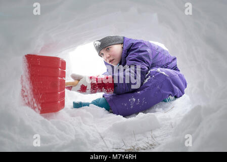 Jeune canadienne à creuser le tunnel de la neige avec une pelle en plastique rouge Banque D'Images