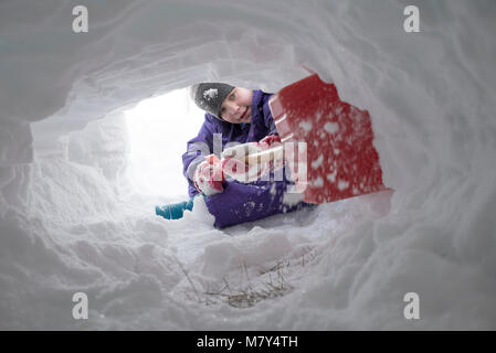 Jeune canadienne à creuser le tunnel de la neige avec une pelle en plastique rouge Banque D'Images