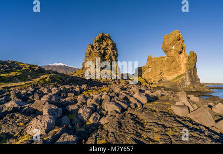 Mer Londrangar-cheminées volcaniques de basalte des digues, dans la distance, Glacier Snaefellsjokull, Péninsule de Snæfellsnes, l'ouest de l'Islande. Banque D'Images