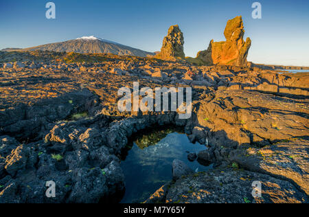 Mer Londrangar-cheminées volcaniques de basalte des digues, dans la distance, Glacier Snaefellsjokull, Péninsule de Snæfellsnes, l'ouest de l'Islande. Banque D'Images