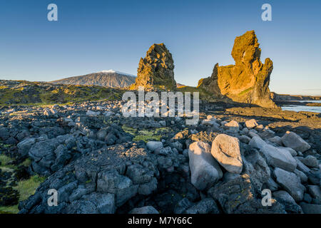 Mer Londrangar-cheminées volcaniques de basalte des digues, dans la distance, Glacier Snaefellsjokull, Péninsule de Snæfellsnes, l'ouest de l'Islande. Banque D'Images