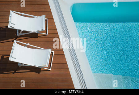 Vue du dessus de chaise longue toile blanche deux chaises placées par une immense piscine turquoise, maison de concept, voyageant ou real estate Banque D'Images