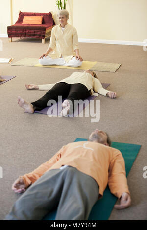 Les jeunes gens pratiquant également appelée relaxation yoga nidra. Guidé par un instructeur certifié de yoga femme pose en shavasana sur theri dos on yoga mat Banque D'Images