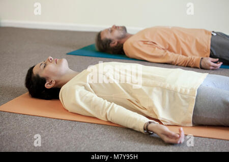 Deux jeunes gens pratiquant également appelée relaxation yoga nidra. En pose shavasana sur leur dos, sur leur tapis de yoga en cours de piscine en li Banque D'Images