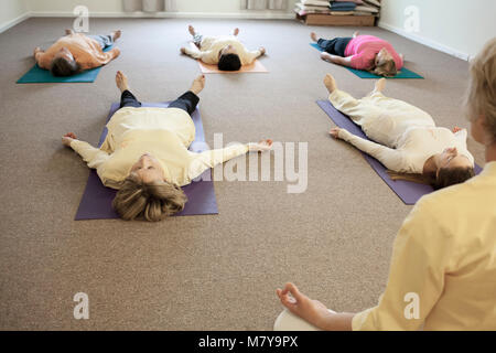 Les jeunes gens pratiquant également appelée relaxation yoga nidra. Guidé par un instructeur certifié de yoga femme pose en shavasana sur theri dos on yoga mat Banque D'Images