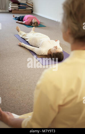 Les jeunes gens pratiquant également appelée relaxation yoga nidra. Guidé par un instructeur certifié de yoga femme pose en shavasana sur theri dos on yoga mat Banque D'Images