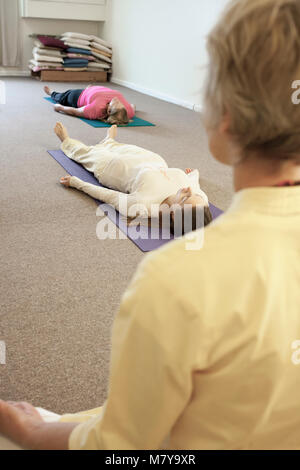 Les jeunes gens pratiquant également appelée relaxation yoga nidra. Guidé par un instructeur certifié de yoga femme pose en shavasana sur theri dos on yoga mat Banque D'Images