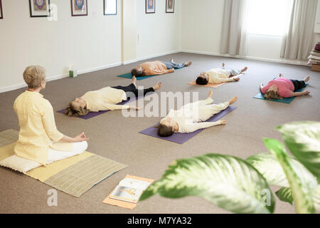 Les jeunes gens pratiquant également appelée relaxation yoga nidra. Guidé par un instructeur certifié de yoga femme pose en shavasana sur theri dos on yoga mat Banque D'Images