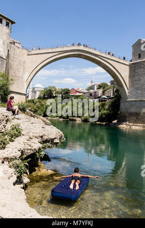 Mostar, Bosnie-Herzégovine, 15 juillet 2017 : Garçon se trouve sur un matelas d'air en face de l'écran historique pont sur la Neretva à Mostar, sur un b Banque D'Images