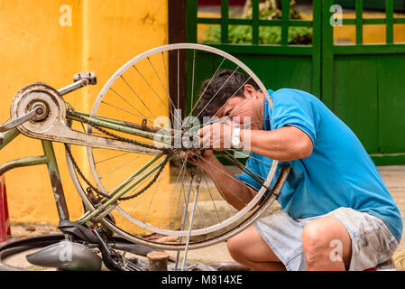 Un homme vietnamien raccommode un vélo dans la rue à Hoi An, Vietnam Banque D'Images