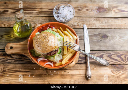 Home-made hamburger au boeuf, tomate et salade sur une plaque avec des pommes de terre rissolées. Fond de bois Banque D'Images