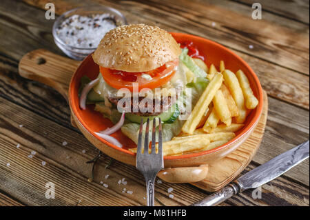 Home-made hamburger au boeuf, tomate et salade sur une plaque avec des pommes de terre rissolées. Fond de bois Banque D'Images