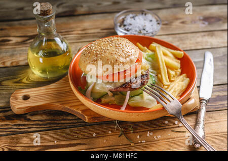 Home-made hamburger au boeuf, tomate et salade sur une plaque avec des pommes de terre rissolées. Fond de bois Banque D'Images