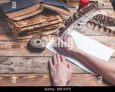 La femelle part écrit la lettre avec plume en plume. Vieux livres, boussole sur un fond de bois. Retro style Banque D'Images