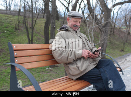 Homme âgé assis sur un banc à l'aide d'une tablette un parc de la ville Banque D'Images