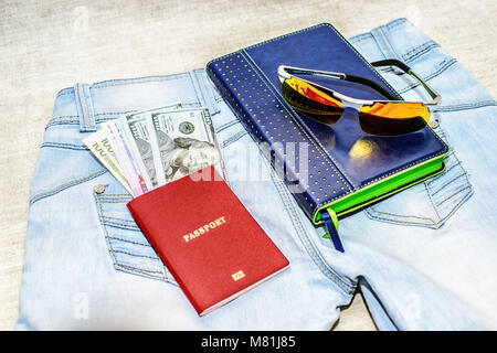 Passeport avec des projets de loi, des verres et le bloc-notes se trouvent sur des jeans. La notion de voyage. Banque D'Images