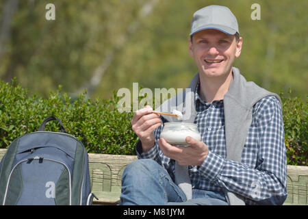 Homme assis sur un banc et de manger du yogourt dans une journée ensoleillée Banque D'Images