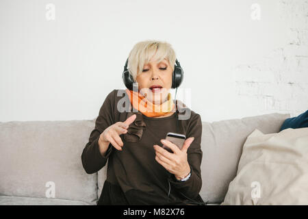Une femme âgée qui écoute de la musique et chante. L'ancienne génération et des nouvelles technologies Banque D'Images