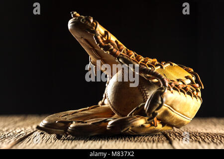 Close up image d'une vieille et baseball baseball glove sur table en bois en arrière-plan noir Banque D'Images