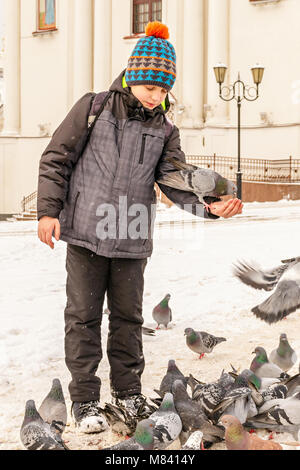 Le garçon nourrit les pigeons sur ses mains, debout sur la place en face de la cathédrale Banque D'Images