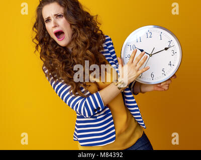 Triste femme élégante en blouson rayé sur fond jaune avec horloge Banque D'Images