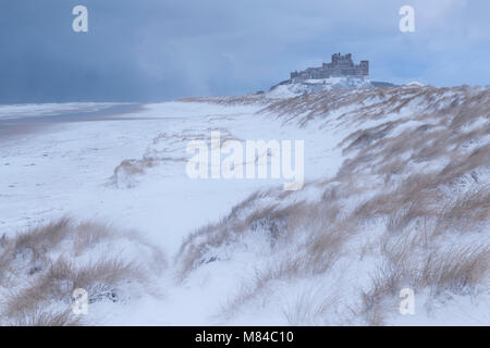 La plage couverte de neige et des dunes de sable par Château de Bamburgh, Northumberland, Angleterre. L'hiver (février) 2018. Banque D'Images