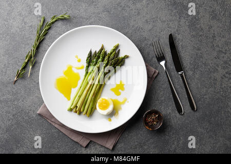 Asperges au four avec oeuf mollet en grande plaque blanche sur fond de pierre, vue du dessus Banque D'Images