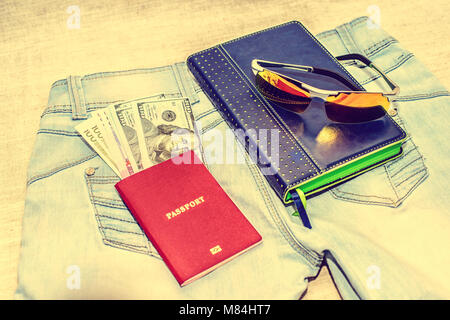 Passeport avec des projets de loi, des verres et le bloc-notes se trouvent sur des jeans. Le concept du voyage Banque D'Images