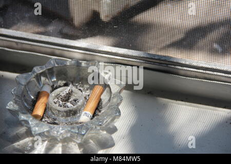 Des cigarettes dans un cendrier en cristal sur l'appui de fenêtre. Banque D'Images