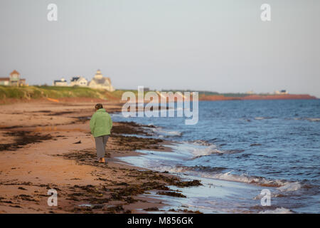 Une femme marche le long du rivage du nord de l'Île du Prince Édouard, Canada au lever du soleil. Banque D'Images