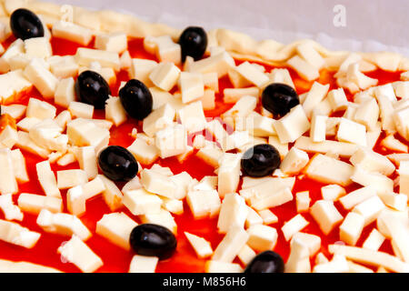 Pizza mozzarella décorée de matières premières, d'olives noires et de la sauce tomate prête à être cuite Banque D'Images