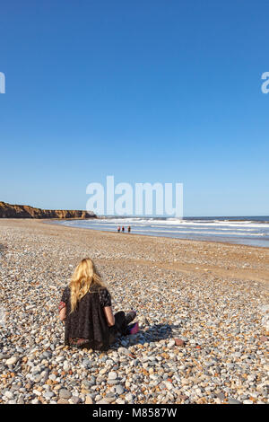 Une femme assise sur la plage à Seaham, County Durham, vers Sunderland. à la fin de l'été soleil et examine sea glass trouvés parmi les cailloux, UK Banque D'Images