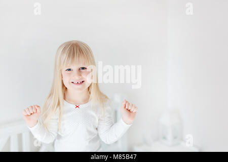 Portrait of little cute girl standing on lit. Sourire Adorable enfant. Kid blonde levant les poings. La victoire ou la réussite des enfants concept Banque D'Images