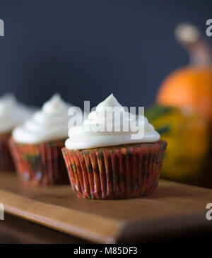 Delicious Pumpkin Spice Cupcakes avec glaçage au fromage à la crème avec des citrouilles en arrière-plan Banque D'Images