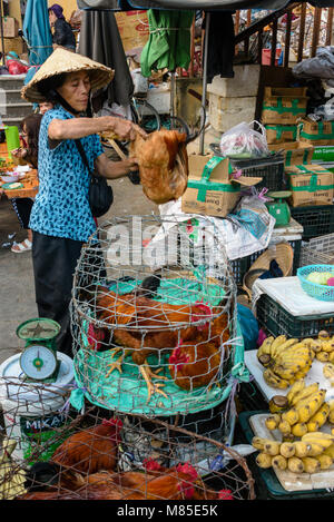 Une femme portant un chapeau conique traditionnel vietnamien bamboo est titulaire d'un chcken par les jambes comme elle le vend à un client à Hoi An, Vietnam Banque D'Images