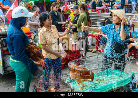 Une femme portant un chapeau conique traditionnel vietnamien bamboo est titulaire d'un chcken par les jambes comme elle le vend à un client à Hoi An, Vietnam Banque D'Images