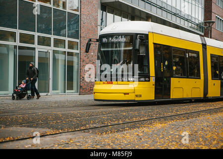 Un tramway moderne jaune descendant la rue. Un père avec un petit enfant marche par. Ville ordinaire de la vie en Europe. Banque D'Images