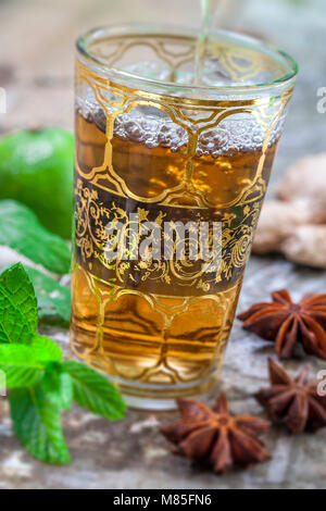 Thé à la menthe nana arabe traditionnel en verre avec la menthe, la cannelle, l'anis étoile sur une vieille planche de bois blanc Banque D'Images