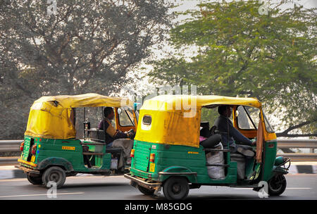 Tuk Tuk est sur une route très fréquentée à Delhi, en Inde. De couleur vert et jaune auto-pousse des déplacements à grande vitesse avec des arbres en arrière-plan Banque D'Images