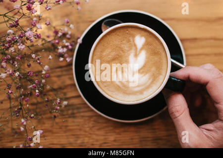 Vue de dessus : une main d'homme est titulaire d'une tasse de café avec des fleurs à proximité, sur une surface en bois. Détendez-vous dans un café, prendre un verre. Banque D'Images