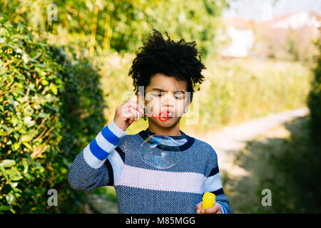 Little Boy blowing bubbles sur un chemin dans le jardin sur une journée ensoleillée Banque D'Images