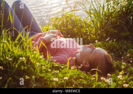 Girl lying on grass par un lac Banque D'Images