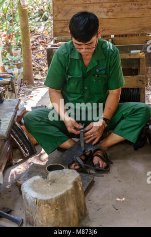 Un homme coupe les vieux pneus afin de faire des sandales au Vietnam. Banque D'Images