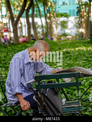 Un chinois de s'asseoir à une table de lire le journal dans Bryant Park, Manhattan, New York City Banque D'Images