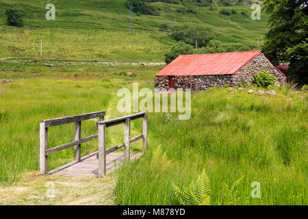 Petit pied en bois pont au-dessus d'un fossé herbeux avec un ancien bâtiment de ferme dans la distance Banque D'Images