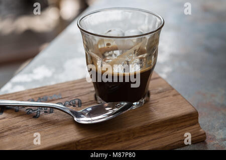 Un double shot d'expresso avec un verre servi sur une planche en bois avec une cuillère. Banque D'Images